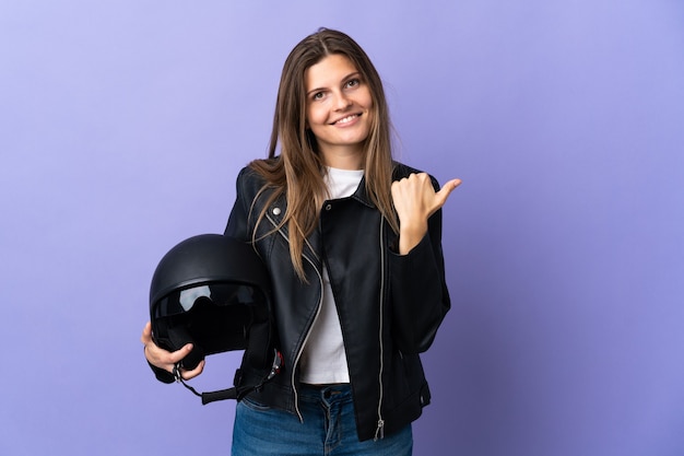 Giovane donna slovacca in possesso di un casco da motociclista isolato su sfondo viola che punta di lato per presentare un prodotto