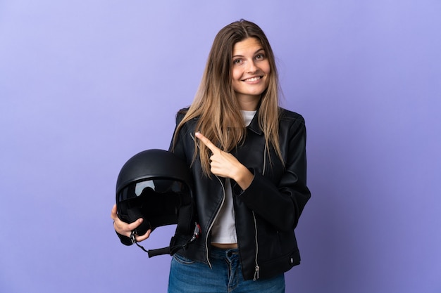 Giovane donna slovacca in possesso di un casco da motociclista isolato su viola che punta di lato per presentare un prodotto