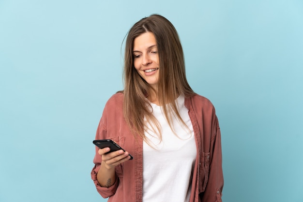 Giovane donna slovacca isolata sulla parete blu che invia un messaggio o un'e-mail con il cellulare