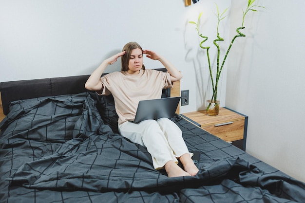 Giovane donna soddisfatta che termina il lavoro sul laptop Ragazza europea seduta con il computer a letto che studia a casa apprendimento a distanza e concetto di lavoro freelance remoto