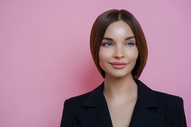 Giovane donna sofisticata con i capelli lisci in un blazer navy equilibrata e elegante su uno sfondo rosa