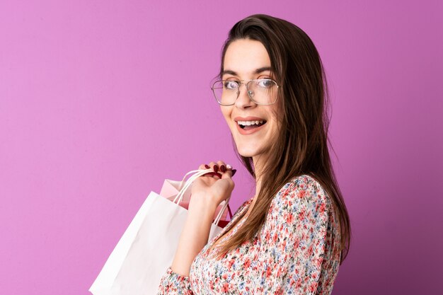 Giovane donna sopra i sacchetti della spesa e sorridere porpora isolati della tenuta della parete