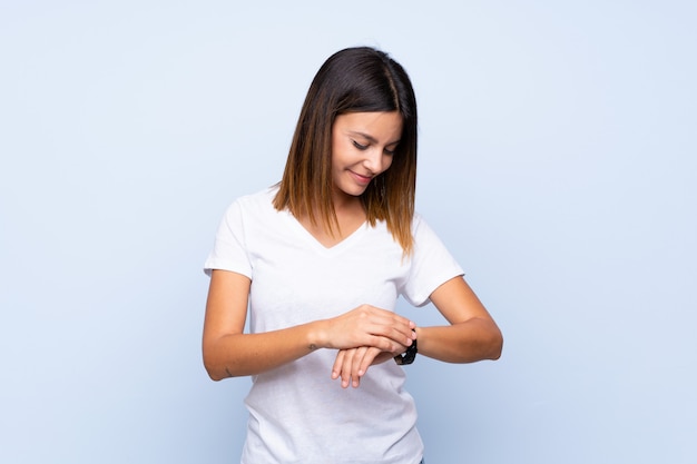 Giovane donna sopra il blu isolato con l'orologio