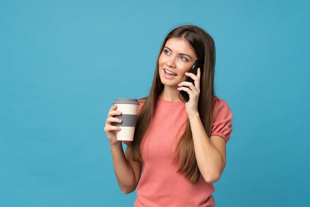 Giovane donna sopra il caffè blu isolato della tenuta da portare via e un cellulare