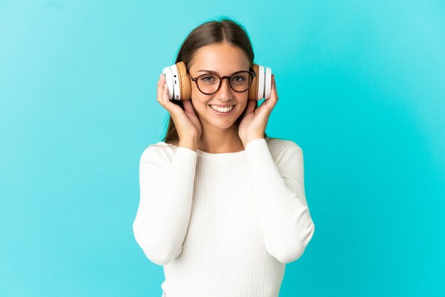 Giovane donna sopra la musica d'ascolto della parete blu isolata