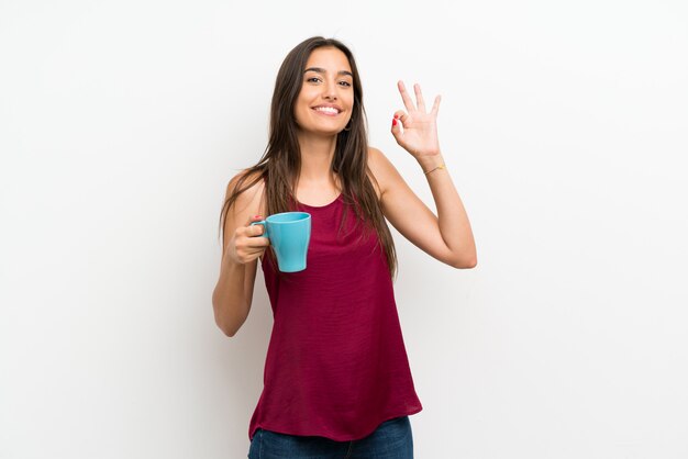 Giovane donna sopra la parete bianca isolata che tiene tazza di caffè calda