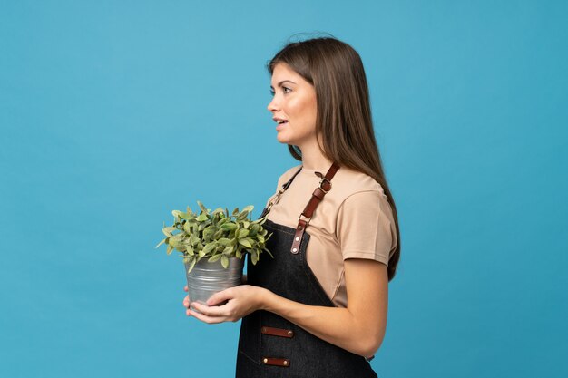 Giovane donna sopra la parete blu isolata che prende un vaso da fiori