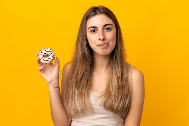 Giovane donna sopra la parete gialla isolata che tiene una ciambella