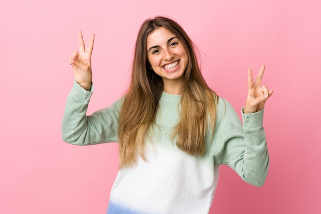 Giovane donna sopra la parete rosa isolata che mostra il segno di vittoria con entrambe le mani