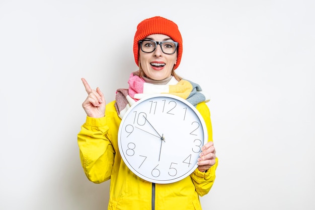 Giovane donna sorpresa che punta il dito verso l'alto tenendo un orologio su uno sfondo chiaro.