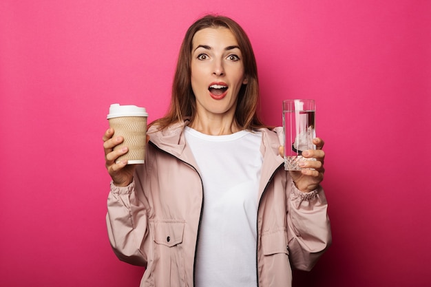 Giovane donna sorpresa che tiene tazza di carta e tazza di vetro con acqua o