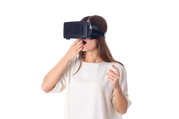 Giovane donna sorpresa in camicia bianca con occhiali per realtà virtuale su sfondo bianco in studio