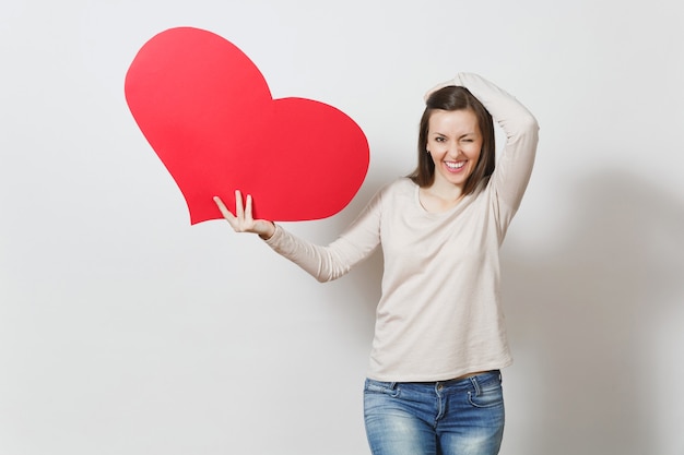 Giovane donna sorridente abbastanza divertente che tiene grande cuore rosso in mani isolate su fondo bianco. Copia spazio per la pubblicità. Con posto per il testo. Concetto di San Valentino o Giornata internazionale della donna.