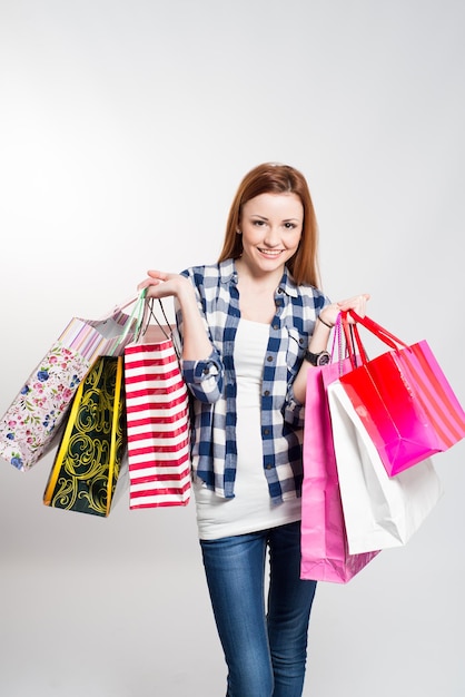 Giovane donna sorridente attraente con molte borse della spesa colorate su grigio. Donna che fa shopping