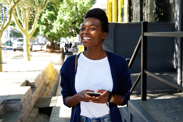 Giovane donna sorridente che cammina con il telefono cellulare e la borsa