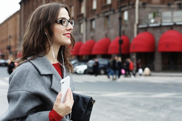 Giovane donna sorridente che chiama e parla su smartphone nella città d'autunno