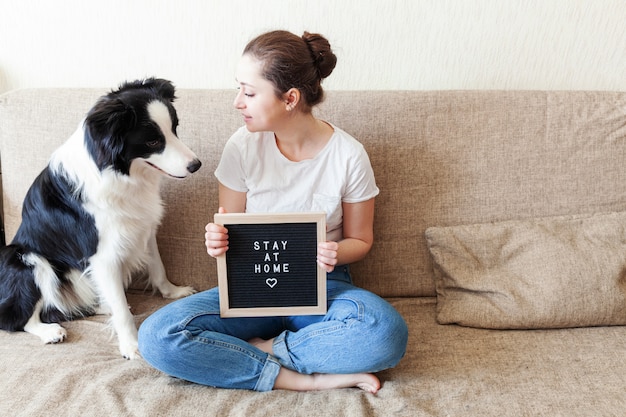 Giovane donna sorridente che gioca con il border collie sveglio del cucciolo di cane sul sofà a casa all'interno