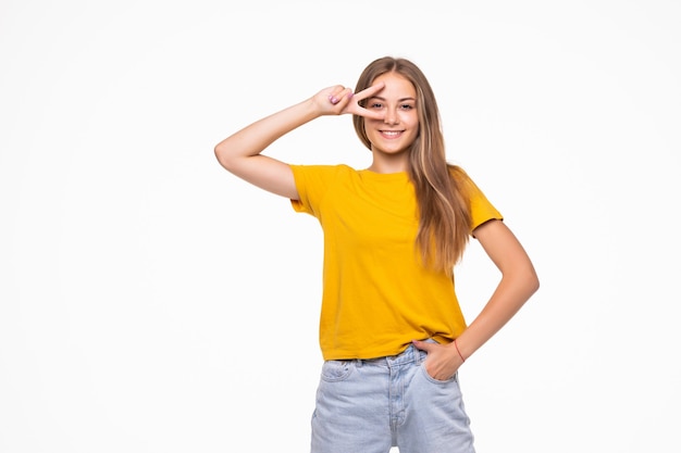 Giovane donna sorridente che mostra la vittoria o il segno di pace isolato sul muro bianco