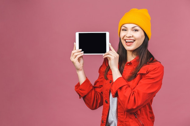 Giovane donna sorridente che mostra lo schermo di computer della compressa isolato sopra la parete rosa.