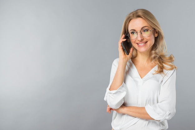 Giovane donna sorridente che parla sul telefono cellulare contro il contesto grigio