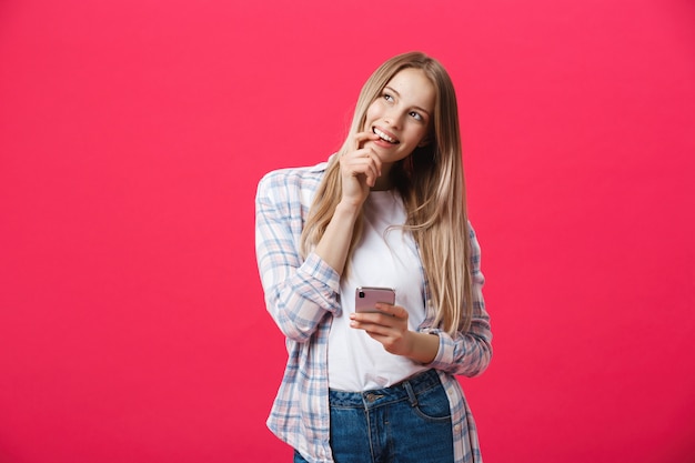 Giovane donna sorridente che pensa mentre usando smartphone.