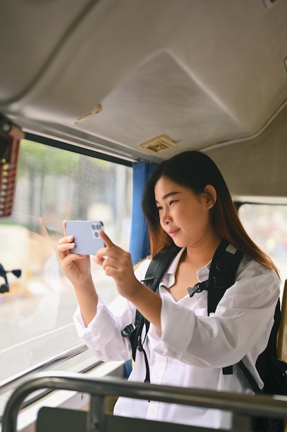 Giovane donna sorridente che scatta foto attraverso la finestra con lo smartphoneConcetto di viaggio e trasporto