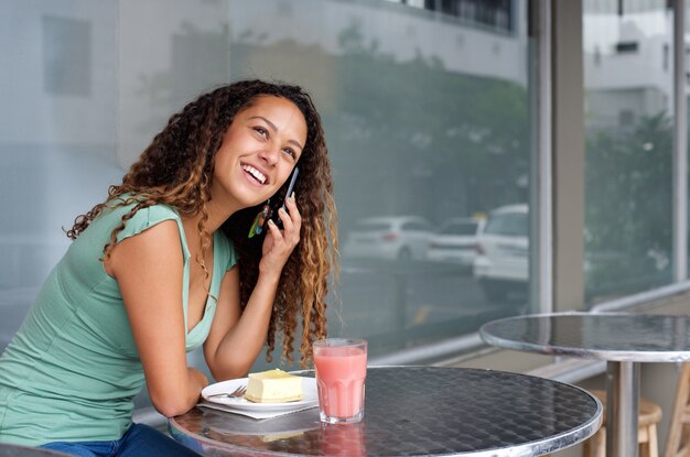 Giovane donna sorridente che si siede ad un ristorante con il telefono cellulare