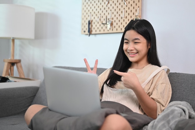 Giovane donna sorridente che si siede sul divano e che ha una videochiamata con il computer portatile.