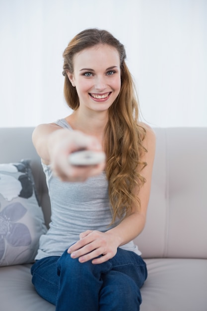 Giovane donna sorridente che si siede sul sofà che guarda TV