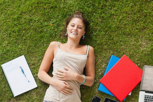 Giovane donna sorridente che si trova sull&#39;erba con i libri