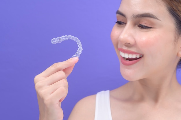 Giovane donna sorridente che tiene bretelle invisalign in studio, assistenza sanitaria dentale e concetto ortodontico