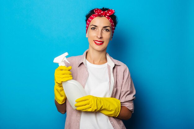 Giovane donna sorridente che tiene spray in guanti su sfondo blu.