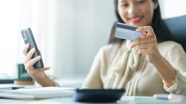 Giovane donna sorridente che utilizza lo smartphone e tiene la carta di credito per fare acquisti online