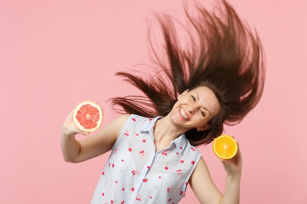 Giovane donna sorridente con capelli svolazzanti che tiene metà di pompelmo fresco maturo, frutta arancione isolata su sfondo rosa pastello. Lo stile di vita vivido delle persone si rilassa il concetto di vacanza. Mock up spazio di copia.