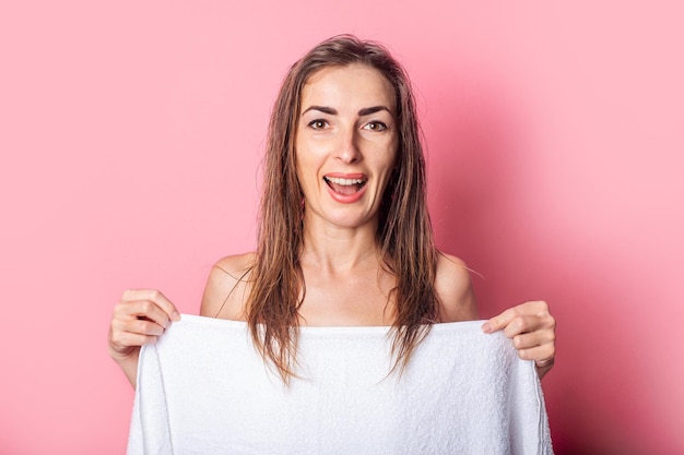 Giovane donna sorridente con i capelli bagnati nudi coperti da un asciugamano su sfondo rosa