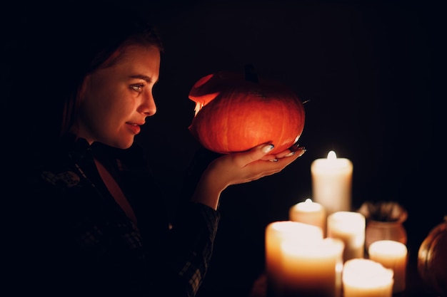 Giovane donna sorridente con la zucca di Halloween Jackolantern testa in mano con le candele Mani femminili che tagliano zucche con un coltello