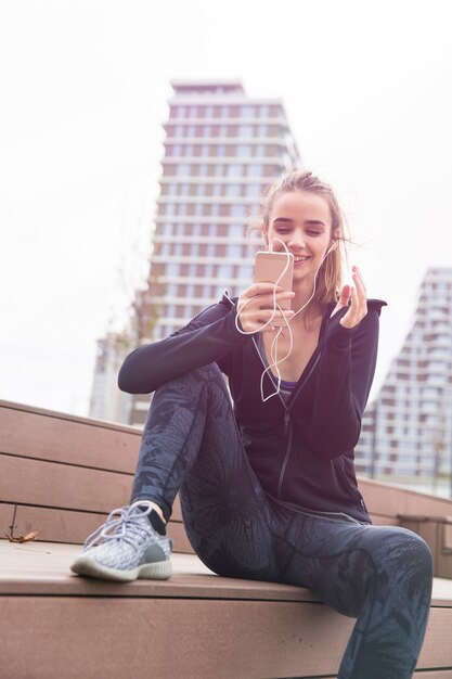 Giovane donna sorridente con lo smartphone e le cuffie che ascolta la musica