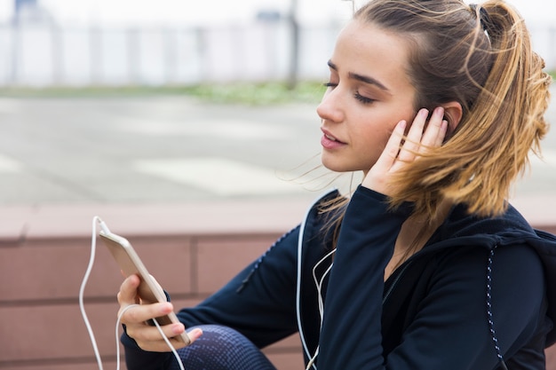 Giovane donna sorridente con lo smartphone e le cuffie che ascolta la musica