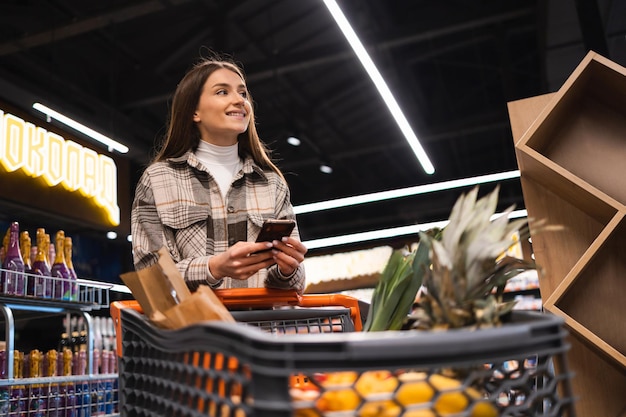 Giovane donna sorridente con lo smartphone nel supermercato