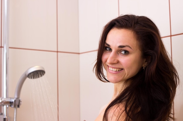 Giovane donna sorridente con lunghi capelli scuri che fa la doccia nel suo bagno chiaro