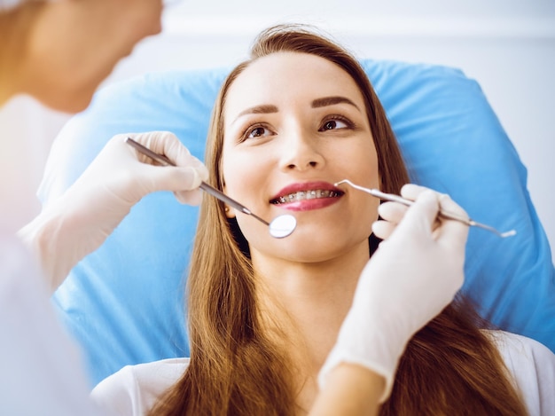 Giovane donna sorridente con parentesi ortodontiche esaminate dal dentista nella soleggiata clinica dentale Denti sani e concetto di medicina