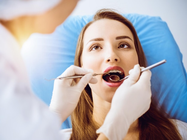 Giovane donna sorridente con parentesi ortodontiche esaminate dal dentista nella soleggiata clinica dentale Denti sani e concetto di medicina