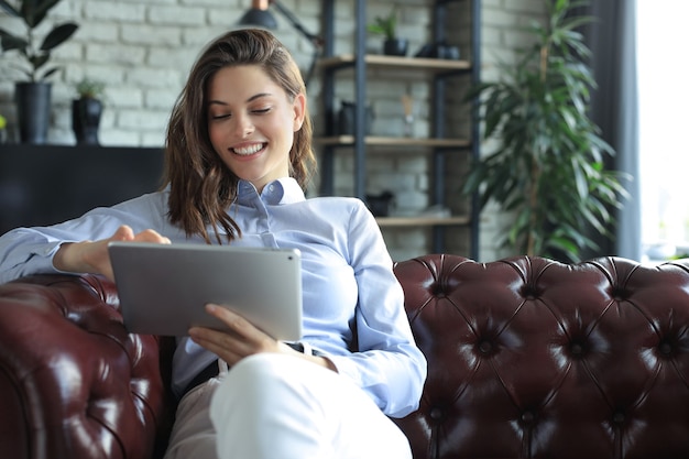 Giovane donna sorridente con tablet pc sul divano.