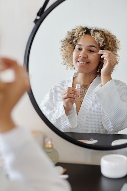 Giovane donna sorridente con un piccolo contagocce che applica il siero sotto la zona degli occhi