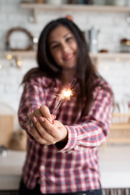 Giovane donna sorridente con una stella filante che celebra il Natale in cucina