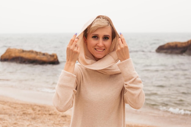 Giovane donna sorridente dei pantaloni a vita bassa che cammina sulla spiaggia sabbiosa vicino al primo piano del mare