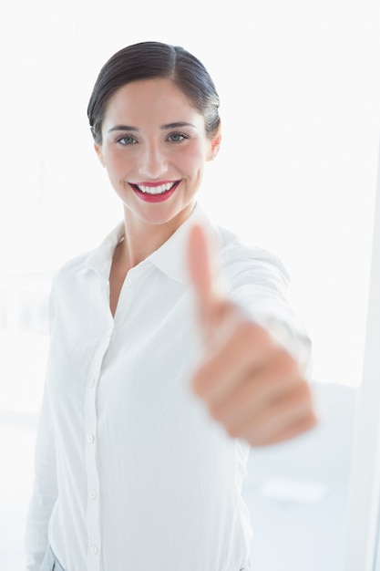 Giovane donna sorridente di affari che gesturing i pollici su