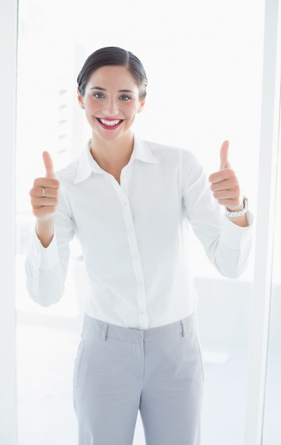 Giovane donna sorridente di affari che gesturing i pollici su