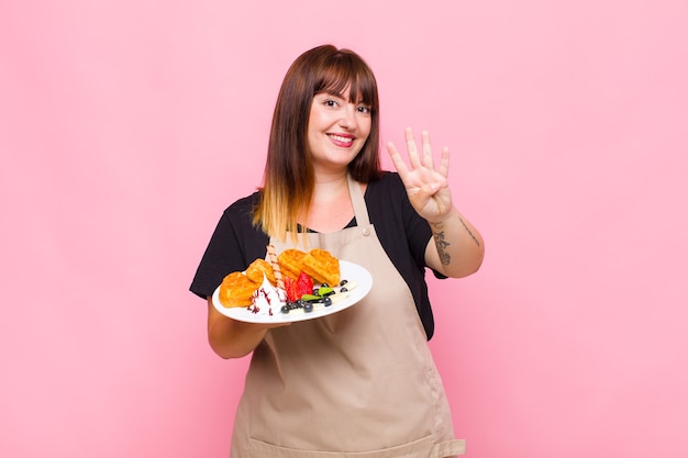 Giovane donna sorridente e dall'aspetto amichevole, mostrando il numero quattro o quarto con la mano in avanti, conto alla rovescia