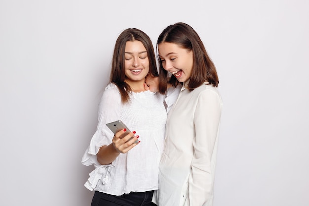 Giovane donna sorridente felice che mostra le foto sul telefono cellulare alla sua amica